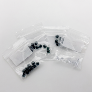 Clear zip-top bags on a white surface containing dark blue-black glass beads; a few beads are loose outside the bags.