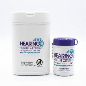 Two white pharmacy-style containers with Hearing Health Center branding; a large tub of antibacterial wipes beside a smaller bottle with a purple cap.